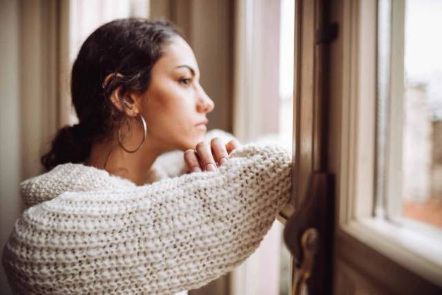 Femme enveloppée dans une couverture et regardant par la fenêtre.