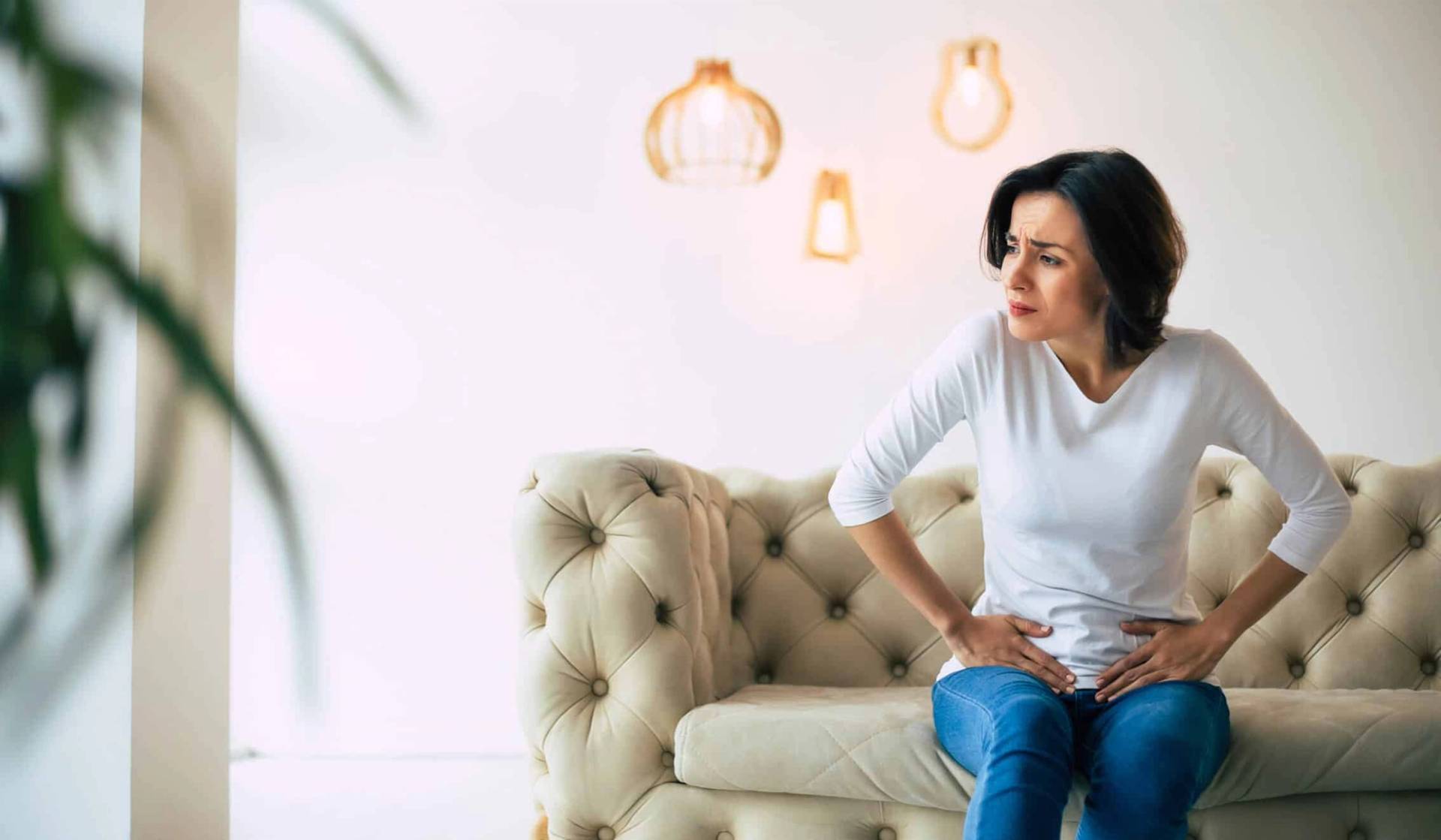 Femme assise sur un canapé, les mains sur le bas-ventre.