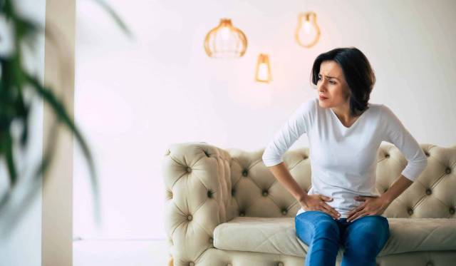 Femme assise sur un canapé, les mains sur le bas-ventre.
