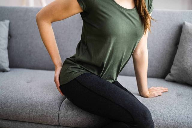 Femme assise sur un canapé avec une main près du bas du dos.