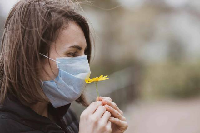 Femme masquée tenant une fleur près du visage.