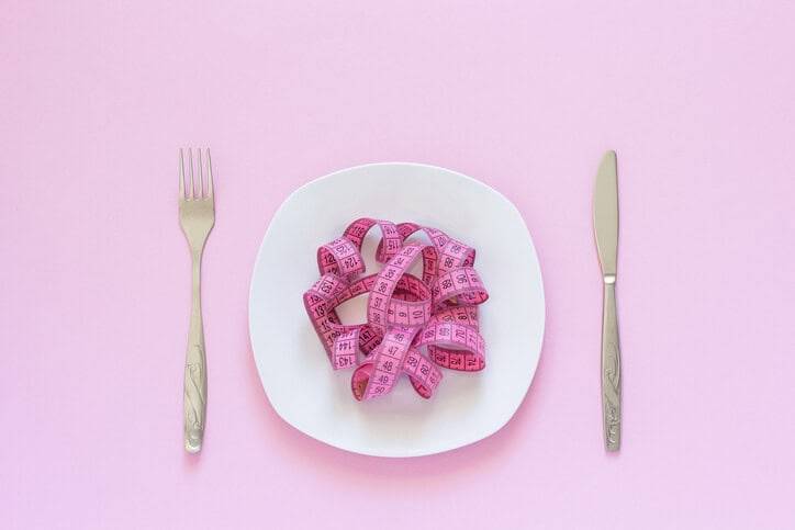 Mètre ruban rose disposé sur une assiette entre des couverts.
