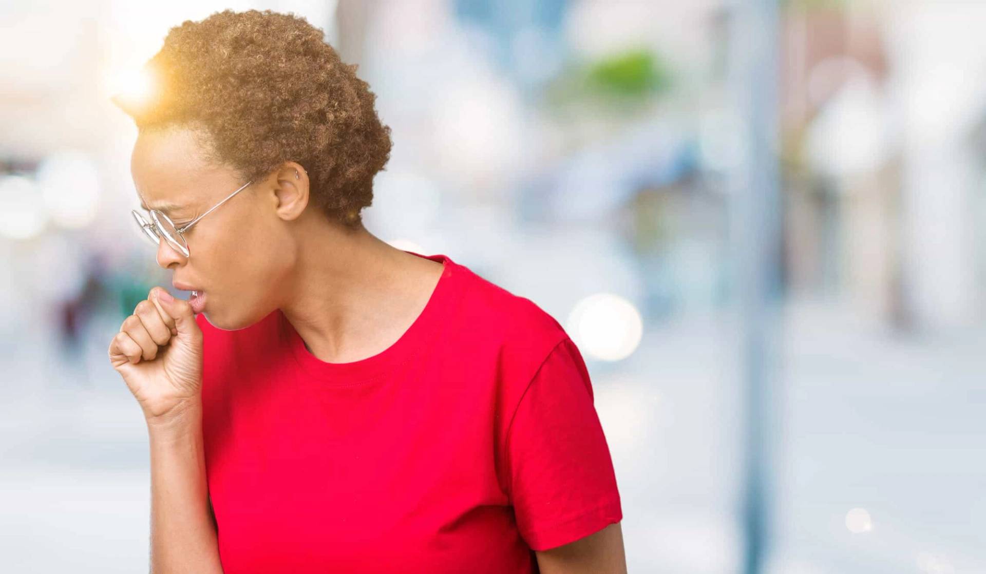 Femme en haut rouge toussant dans sa main.