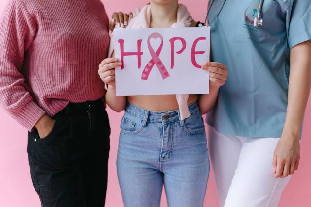 Trois femmes tenant un panneau 'ESPOIR' avec un ruban rose pour sensibiliser au cancer du sein