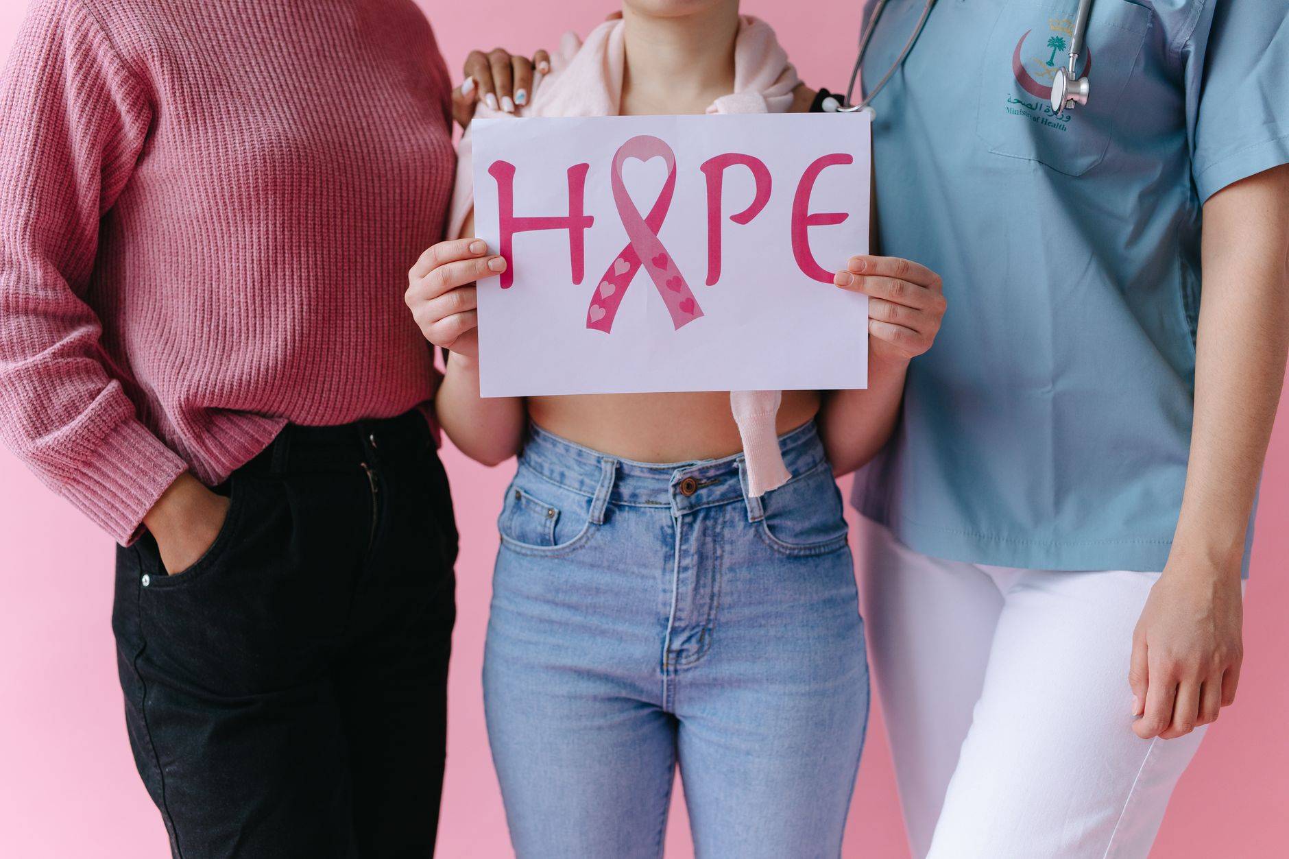 Trois femmes tenant un panneau 'ESPOIR' avec un ruban rose pour sensibiliser au cancer du sein