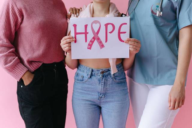 Trois femmes tenant un panneau 'ESPOIR' avec un ruban rose pour sensibiliser au cancer du sein
