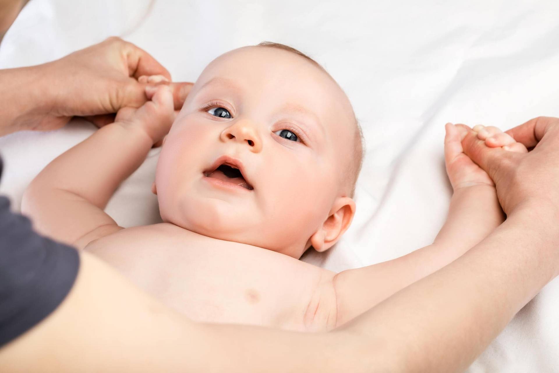 Bébé allongé dont un adulte tient les deux mains.