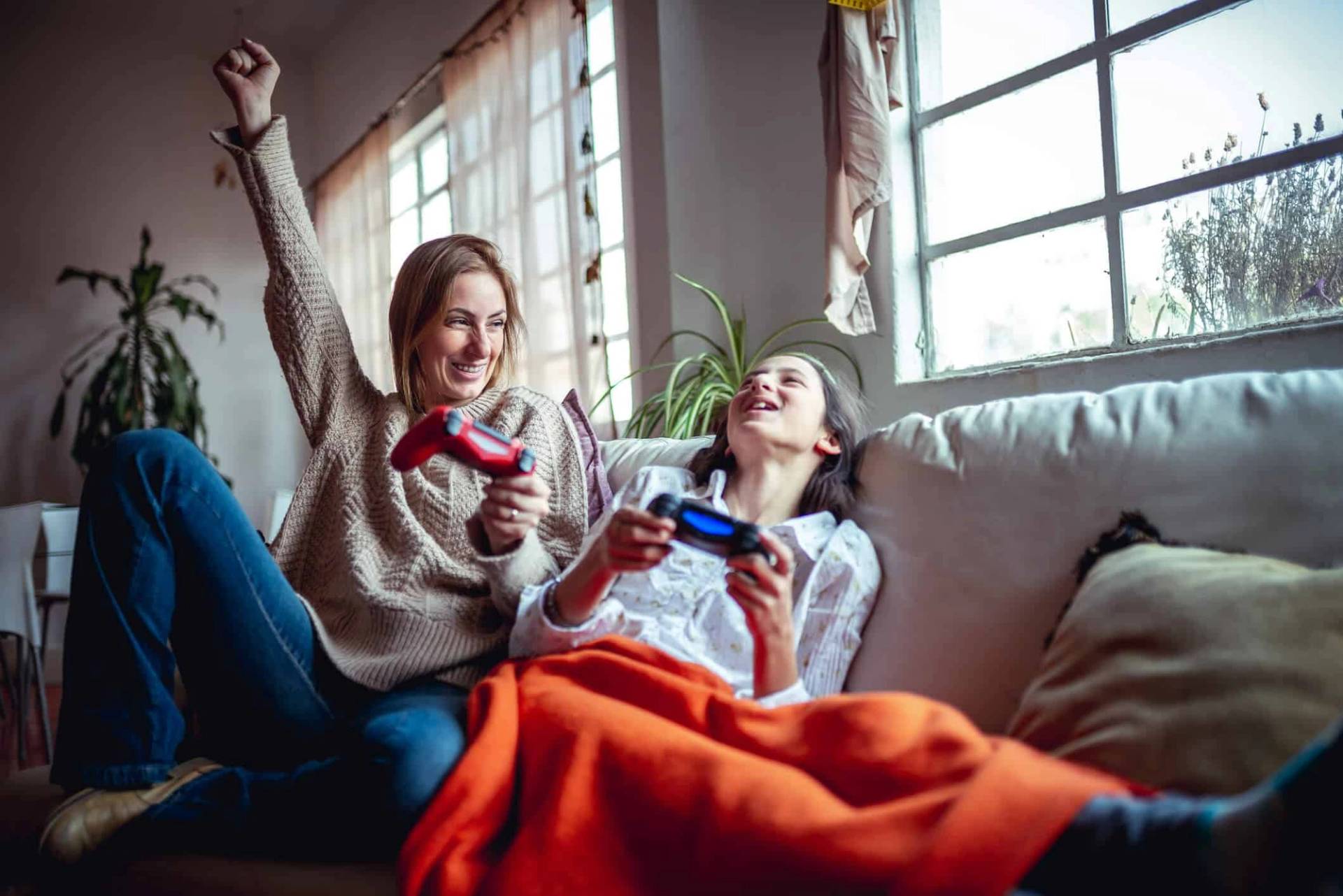Adulte et adolescente jouant à la console sur un canapé.