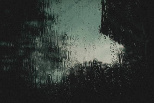 Capture artistique de gouttes de pluie sur verre avec une atmosphère sombre et moody. Idéal pour les arrière-plans