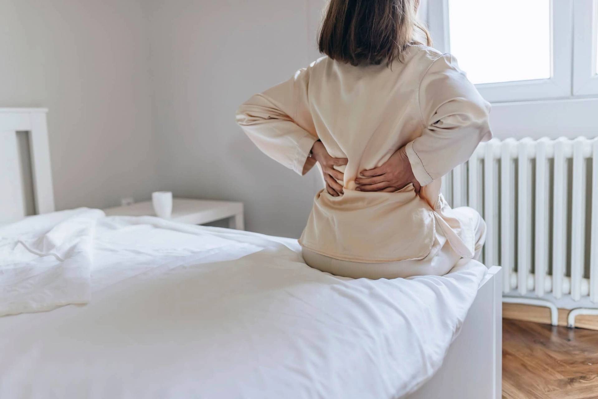 Femme de dos sur un lit, mains sur les lombaires.