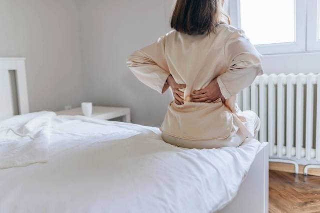 Femme de dos sur un lit, mains sur les lombaires.