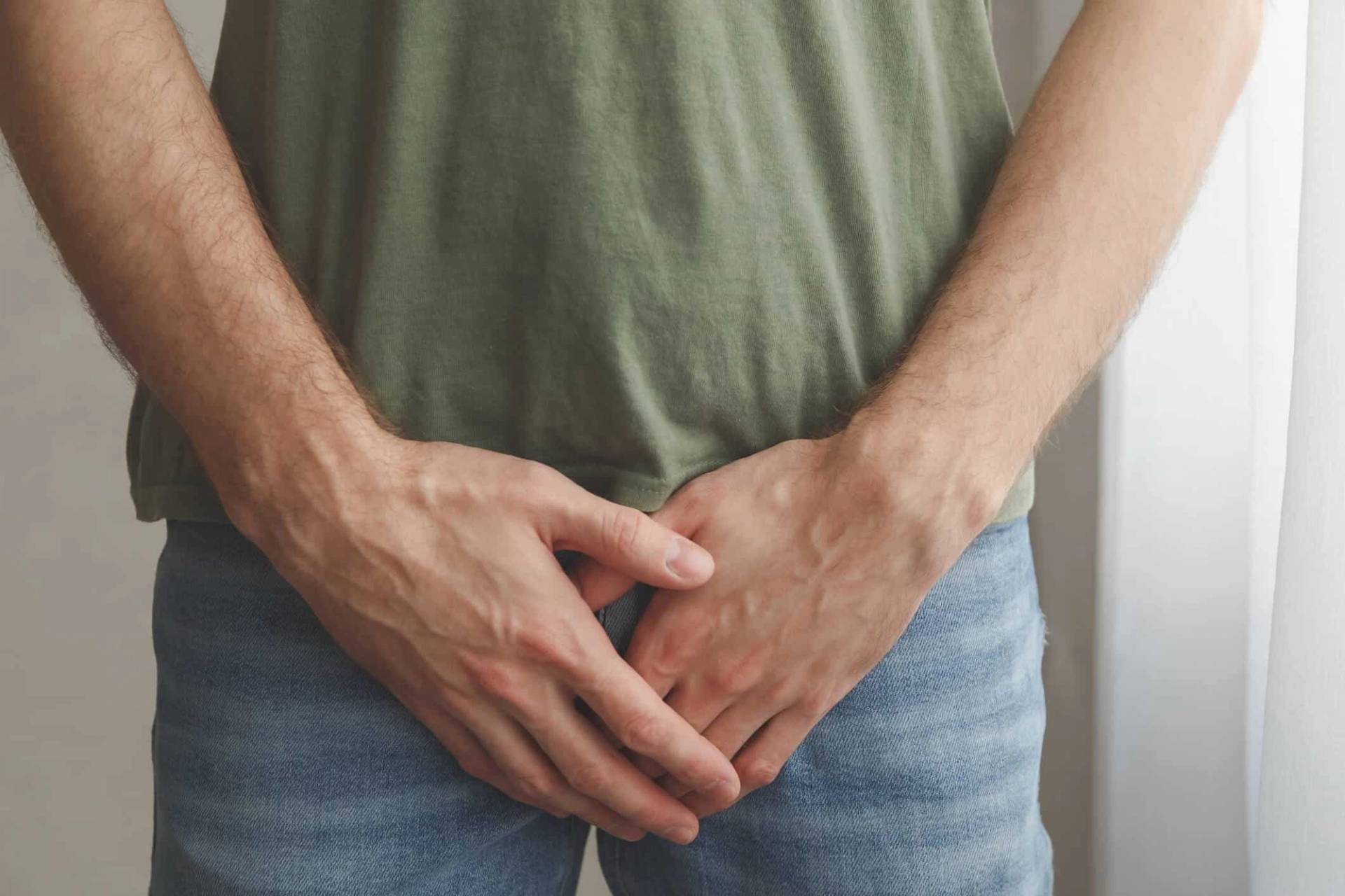 Homme debout les mains devant l’entrejambe.
