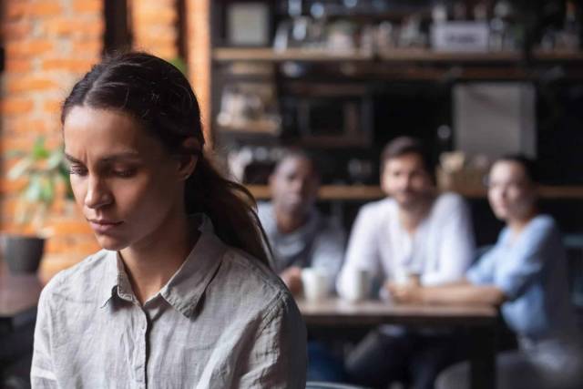 Femme préoccupée au premier plan, avec un groupe assis à une table derrière elle.