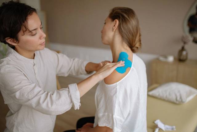 Un physiothérapeute applique du tape kinésiologique bleu sur l'épaule d'un patient pour soutenir les muscles