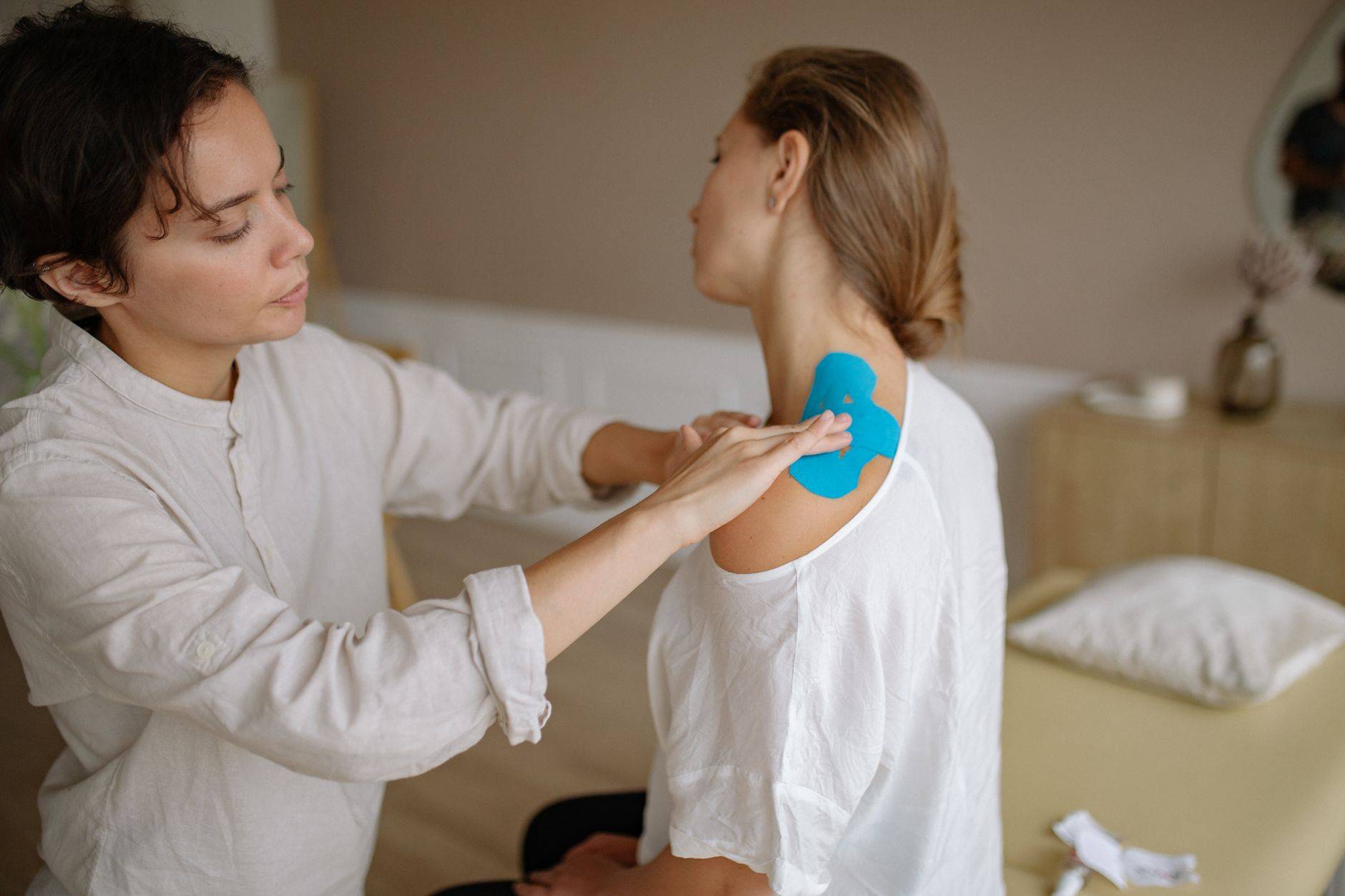 Un physiothérapeute applique du tape kinésiologique bleu sur l'épaule d'un patient pour soutenir les muscles