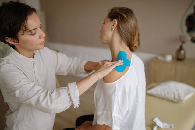 Un physiothérapeute applique du tape kinésiologique bleu sur l'épaule d'un patient pour soutenir les muscles