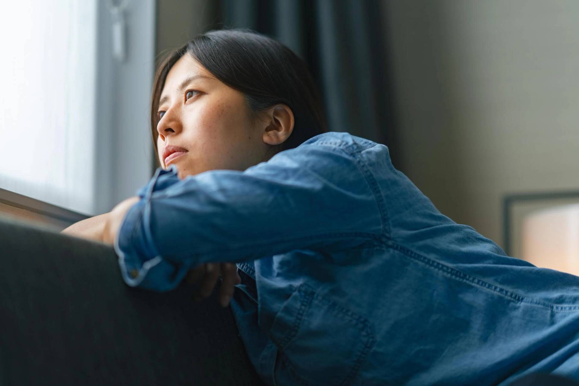 Femme songeuse adossée près d’une fenêtre.