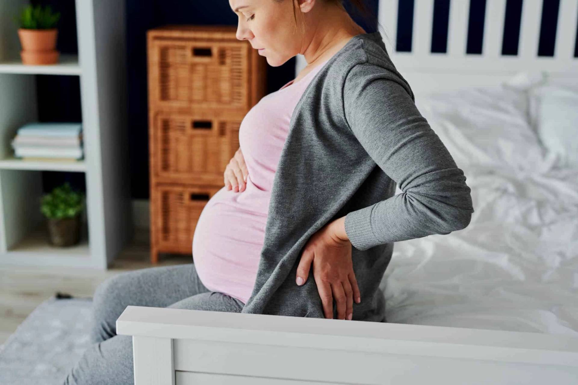 Femme enceinte assise, une main dans le bas du dos.