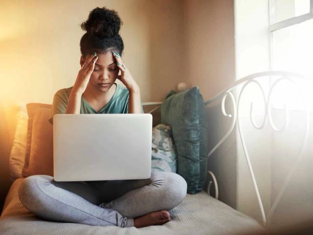 Femme assise devant un ordinateur portable, les mains aux tempes.