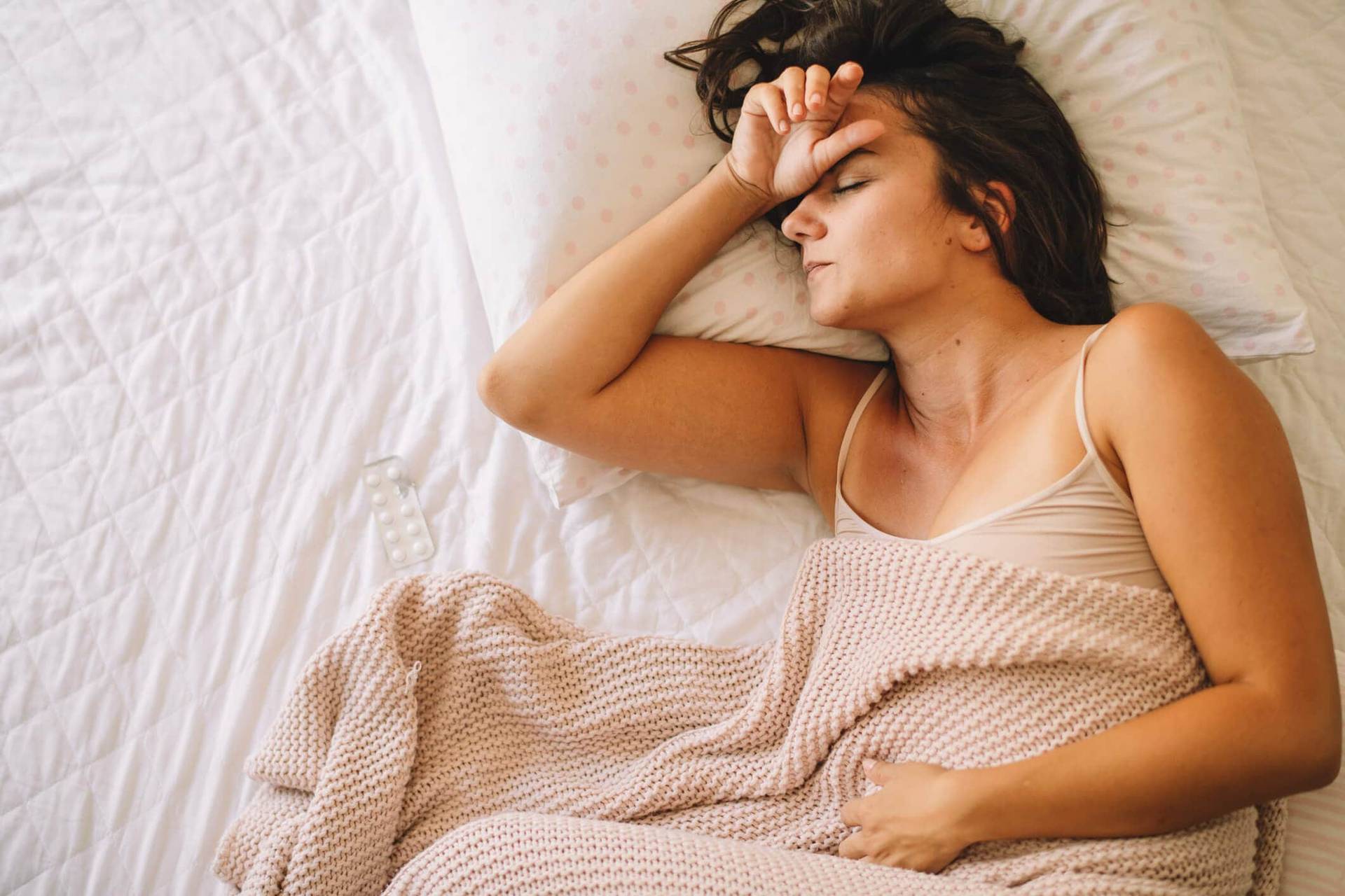 Femme allongée sur un lit, une main au front.