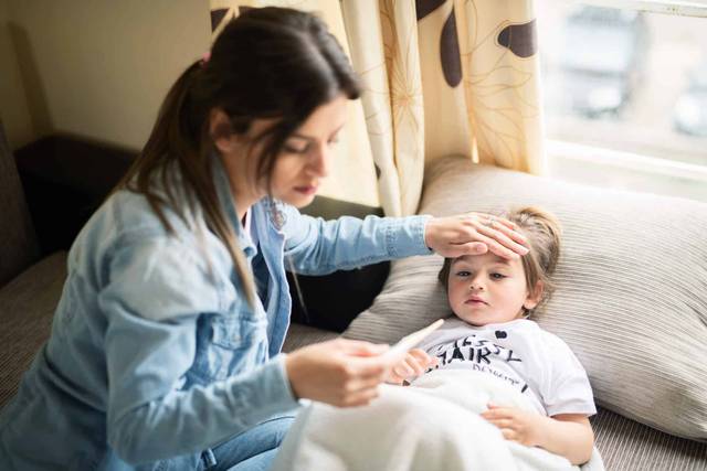 Adulte prenant la température d’un enfant sur un canapé.