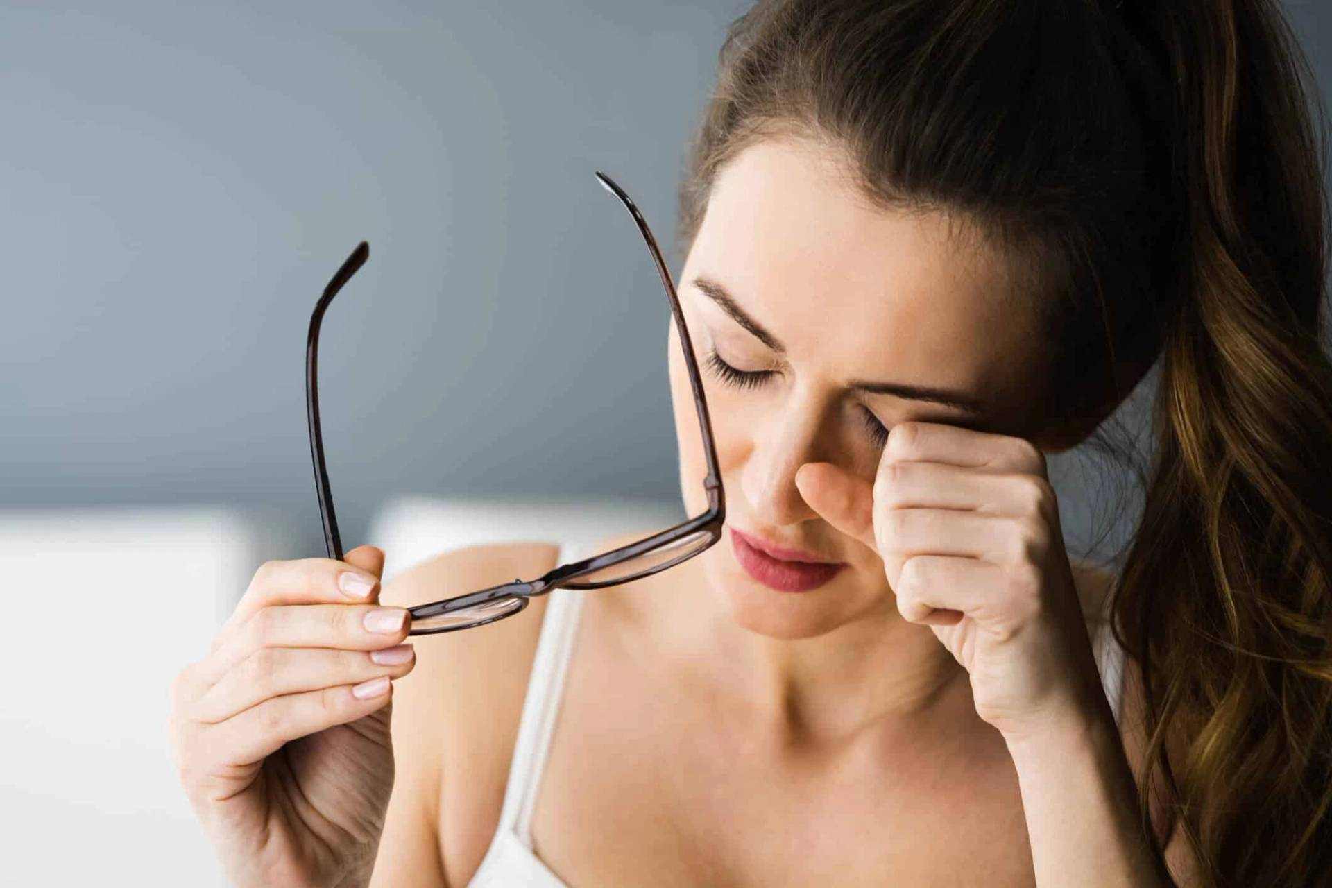 Femme retirant ses lunettes et frottant son œil.