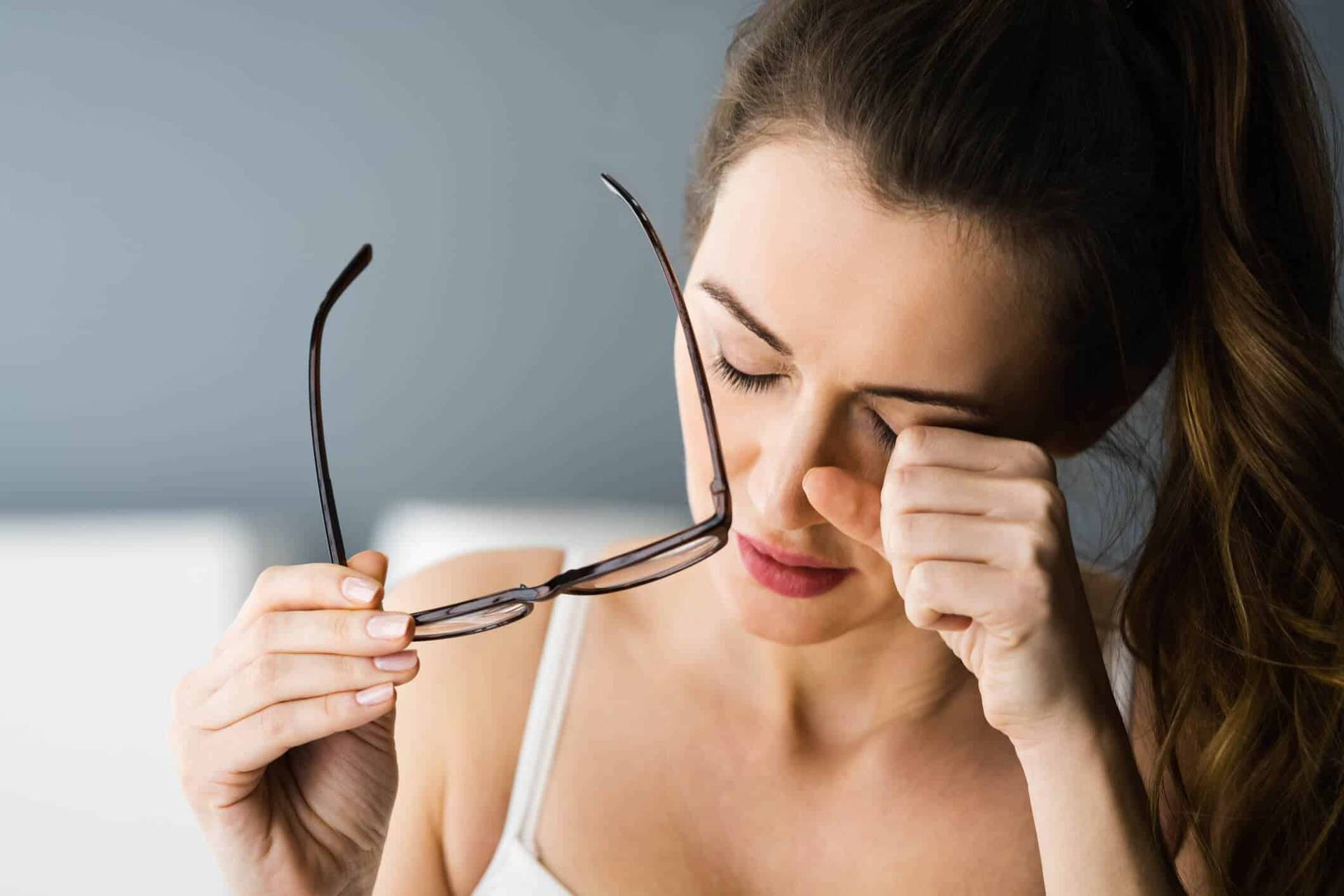 Femme retirant ses lunettes et frottant son œil.