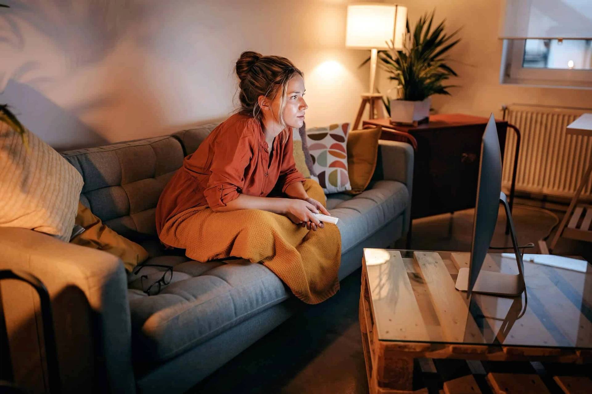 Femme jouant à un jeu vidéo sur un canapé le soir.