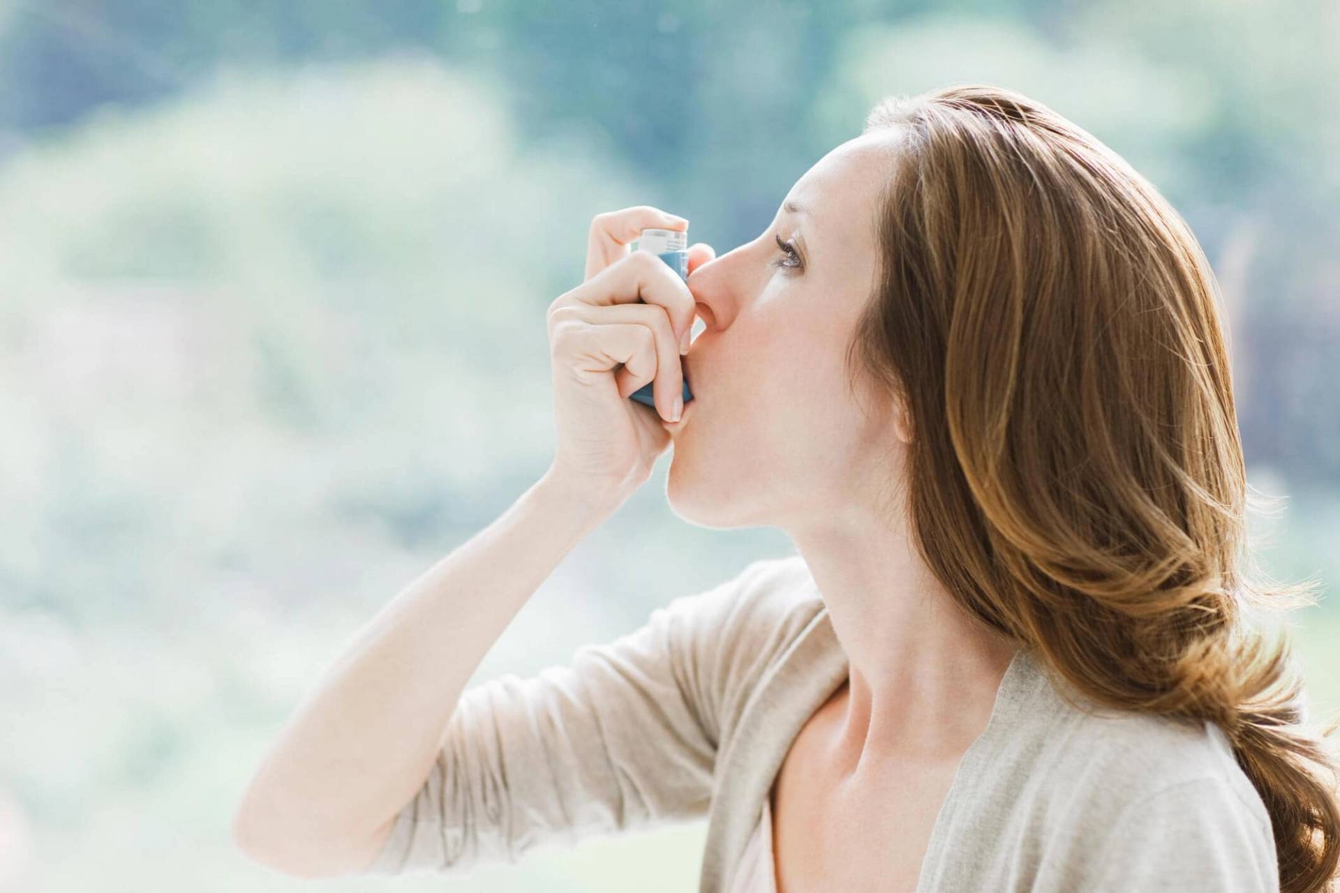 Femme utilisant un inhalateur près d’une fenêtre.