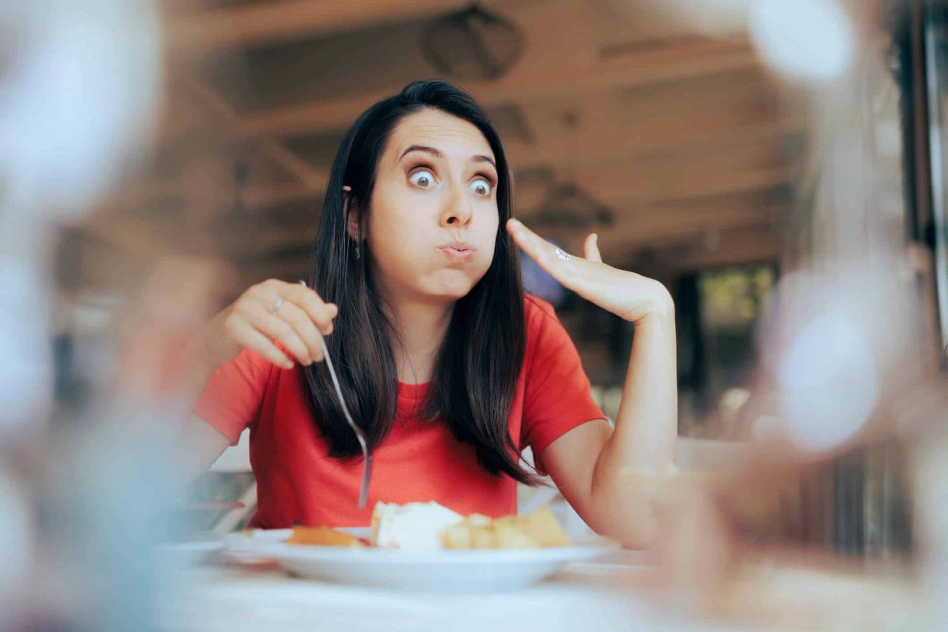 Femme à table faisant un geste vers sa bouche après une bouchée.