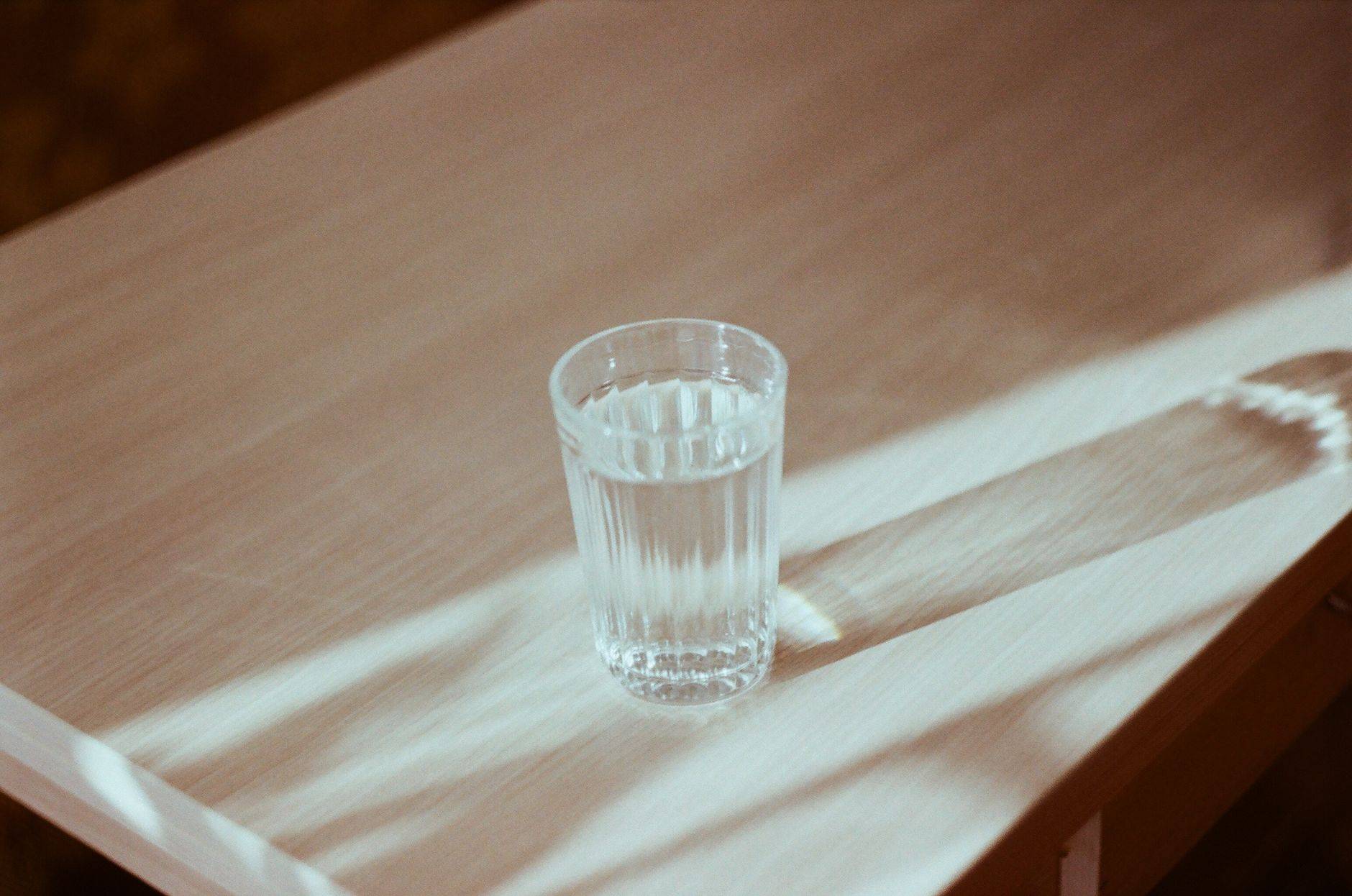Verre d’eau posé sur une table en bois éclairée par le soleil.