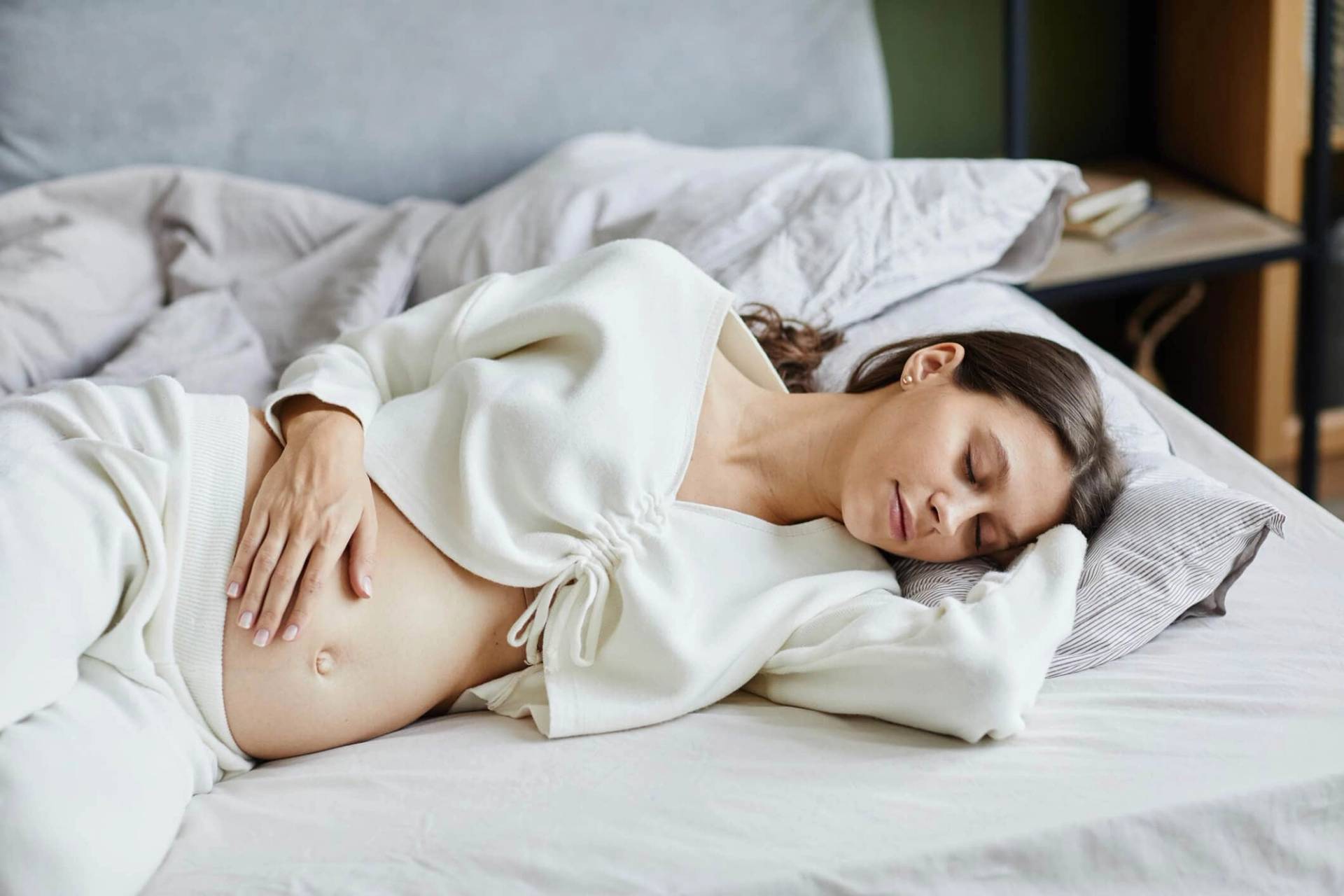 Femme enceinte allongée sur un lit, une main sur le ventre.