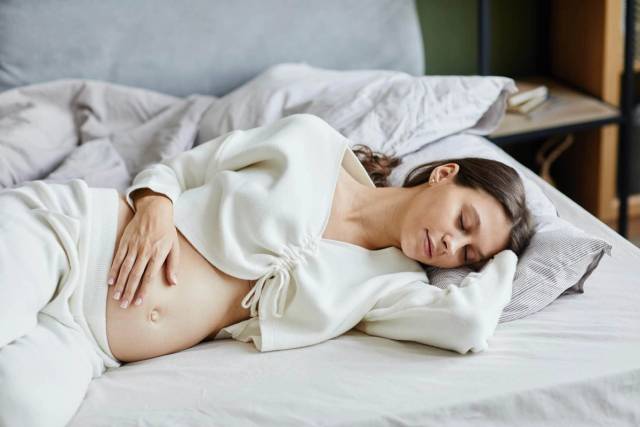 Femme enceinte allongée sur un lit, une main sur le ventre.