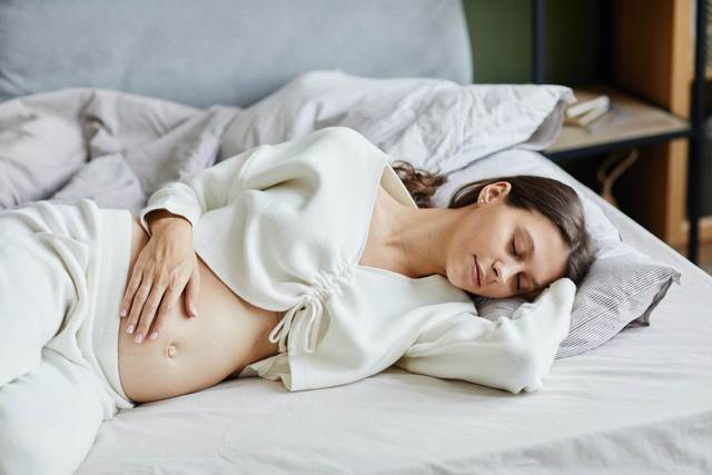 Femme enceinte allongée sur un lit, une main sur le ventre.