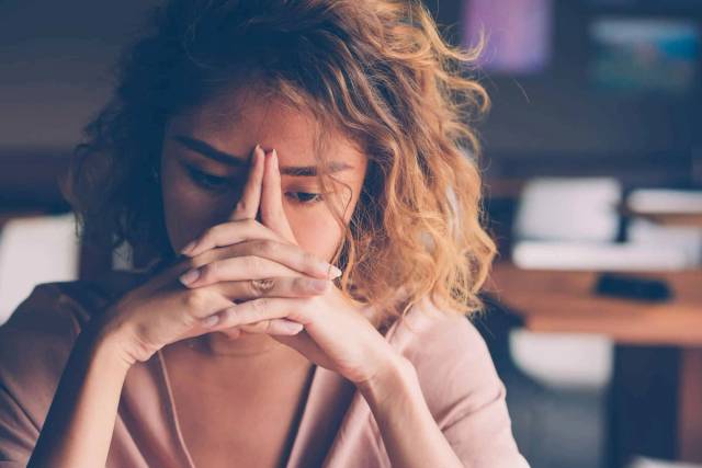 Femme au bureau, mains jointes devant son visage et sourcils froncés.