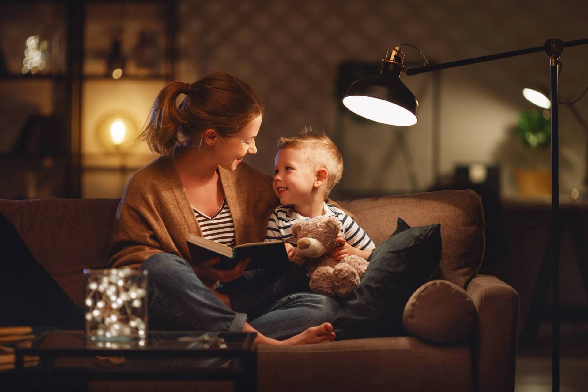 Adulte lisant avec un jeune enfant sur un canapé.
