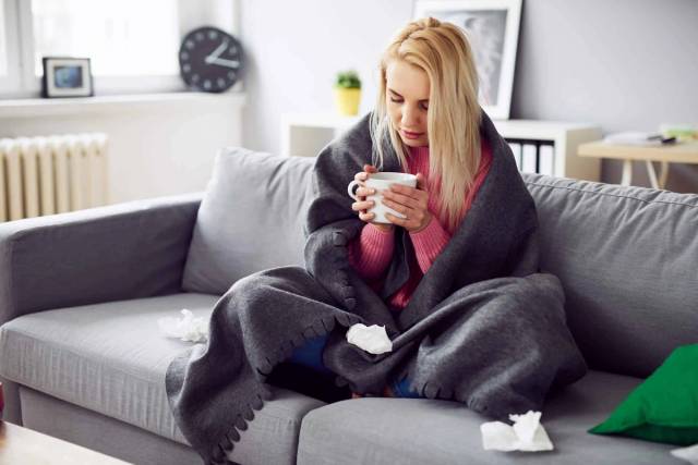 Femme enveloppée dans une couverture tenant une tasse.