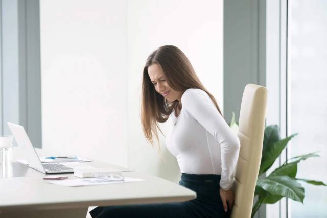 Femme assise au bureau, main placée derrière le bassin.