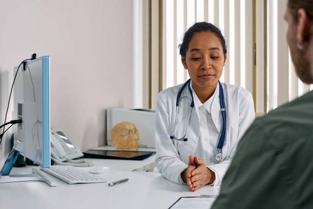 Une médecin en blouse blanche échange avec une personne assise face à elle dans son cabinet.