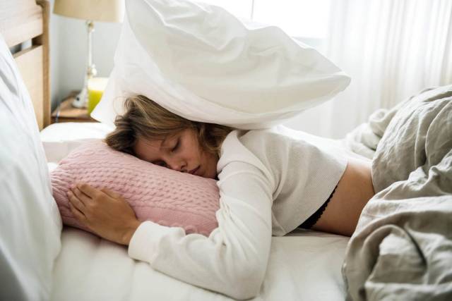 Femme allongée sur un lit avec un oreiller sur la tête.
