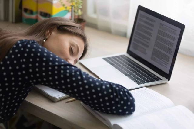 Femme endormie sur ses bras à côté d’un ordinateur portable.