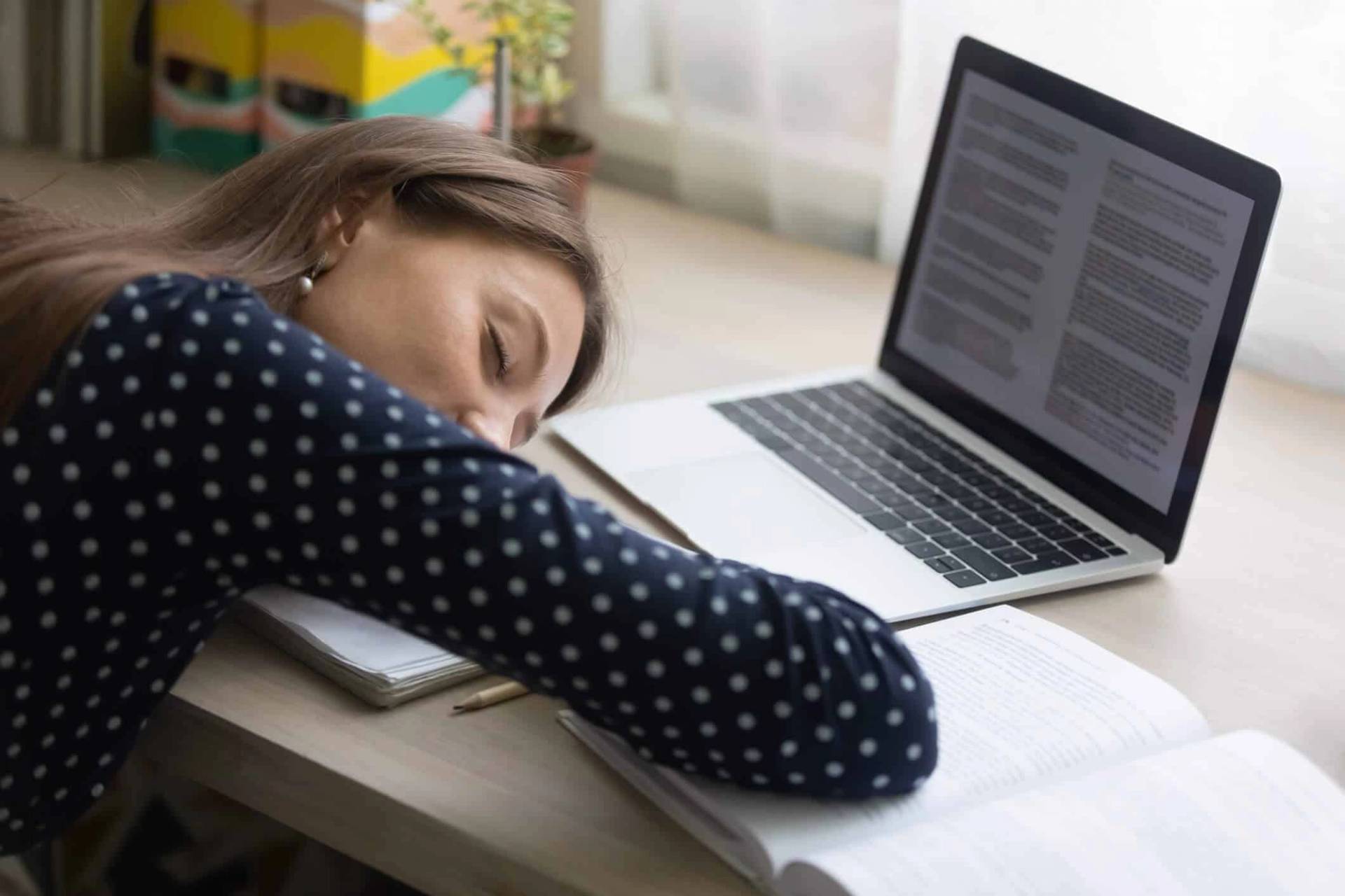 Femme endormie sur ses bras à côté d’un ordinateur portable.