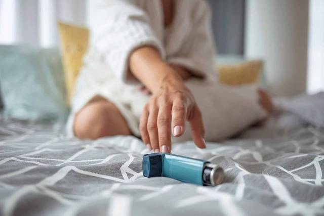 Main d’un adulte saisissant un inhalateur posé sur un lit.