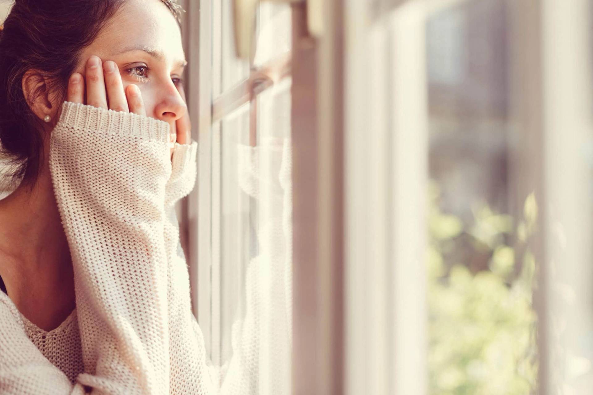 Femme regardant par une fenêtre, une main contre sa joue.