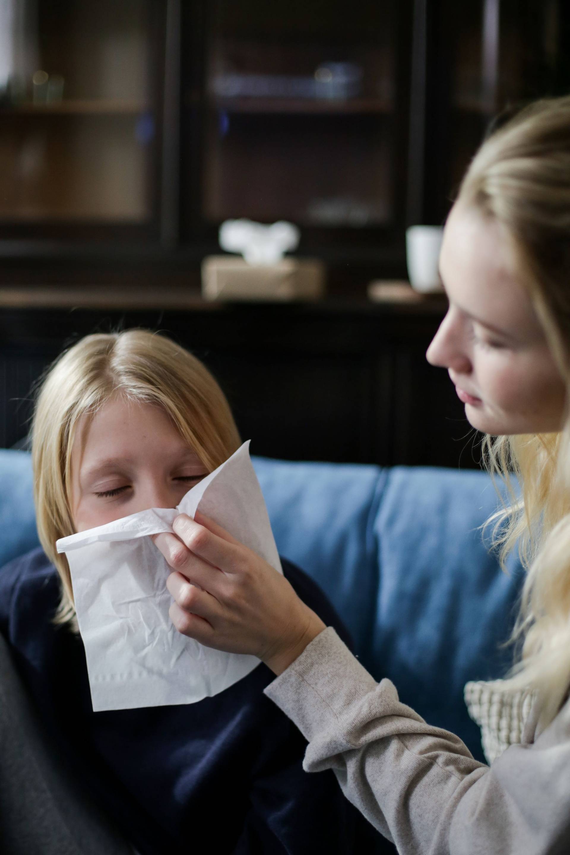 Une mère essuie le nez de son enfant avec un mouchoir, sur un canapé.