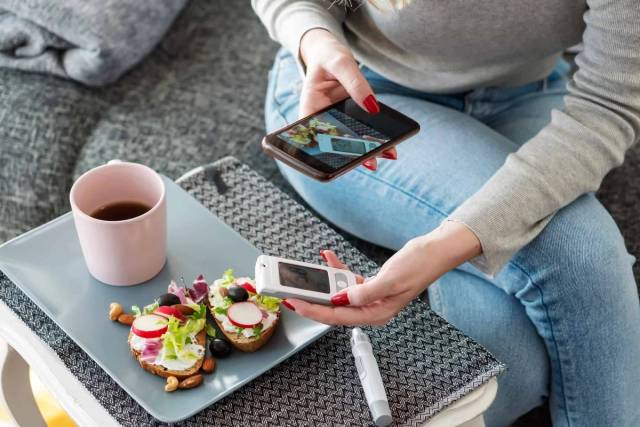 Personne tenant un lecteur de glycémie et un téléphone près d’un repas.
