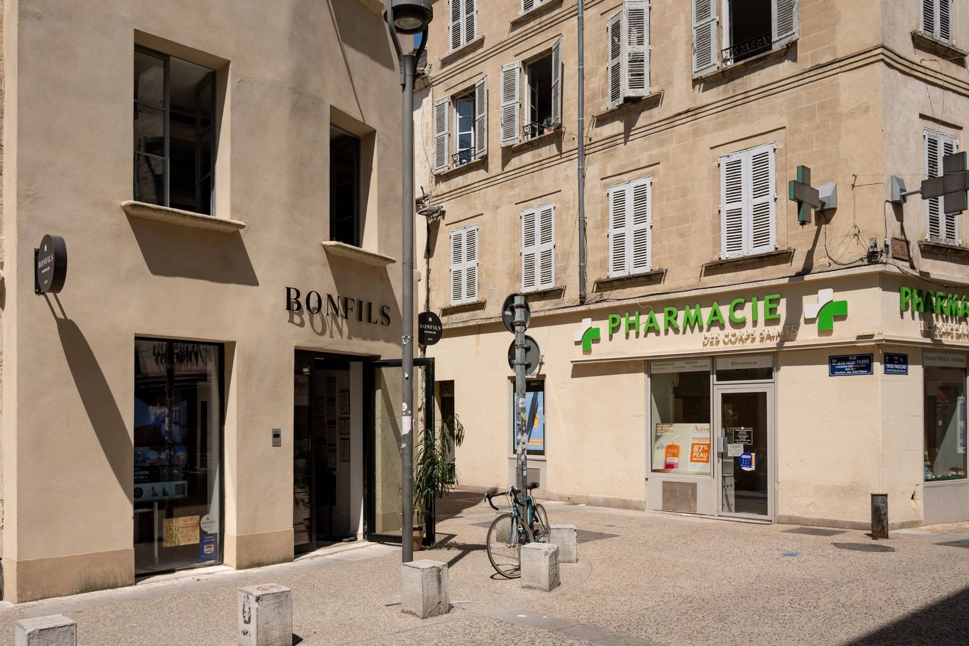 Façade d’une pharmacie dans une rue, avec son enseigne et sa croix.