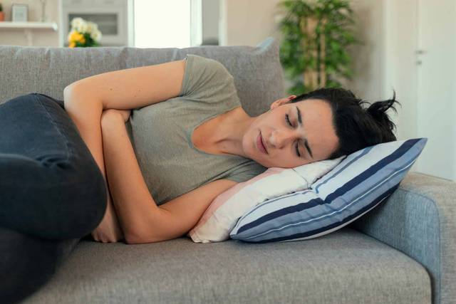 Femme allongée sur un canapé, les bras contre le ventre.