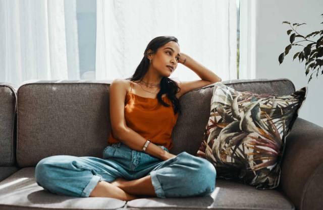 Femme assise sur un canapé, une main près de la tempe.