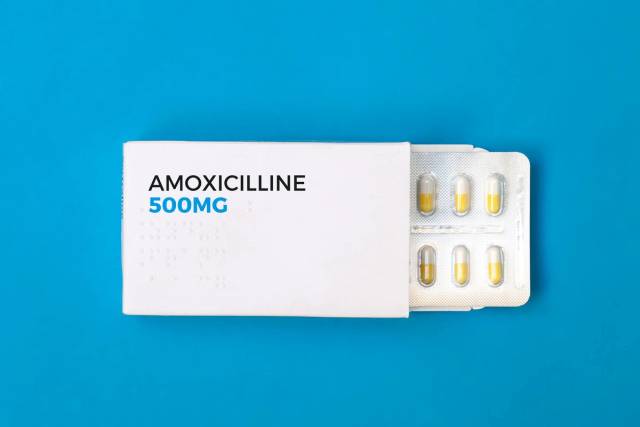 Boîte blanche portant Amoxicilline 500 mg avec une plaquette de gélules sur fond bleu.